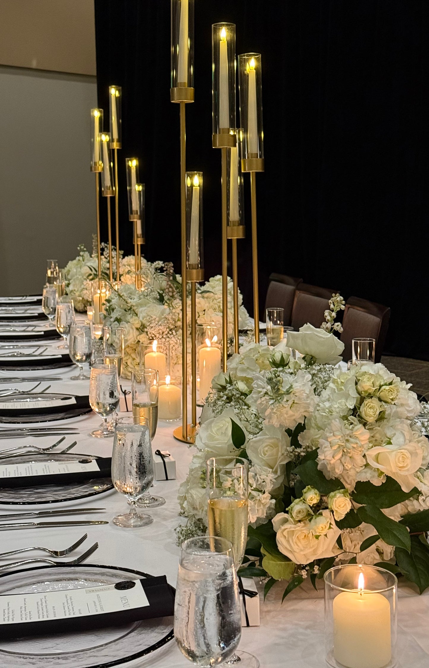 Elegant table setting with candles, flowers, and glassware on a white tablecloth.