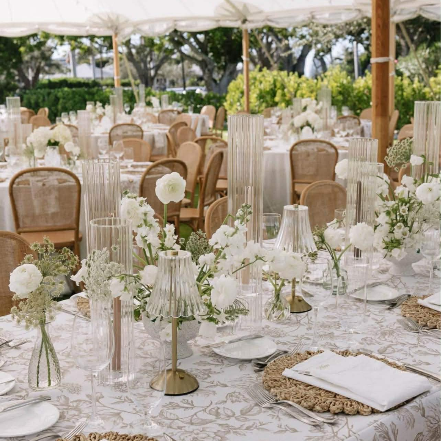 Elegant wedding reception with tables set for dinner, white flowers, and clear glassware.