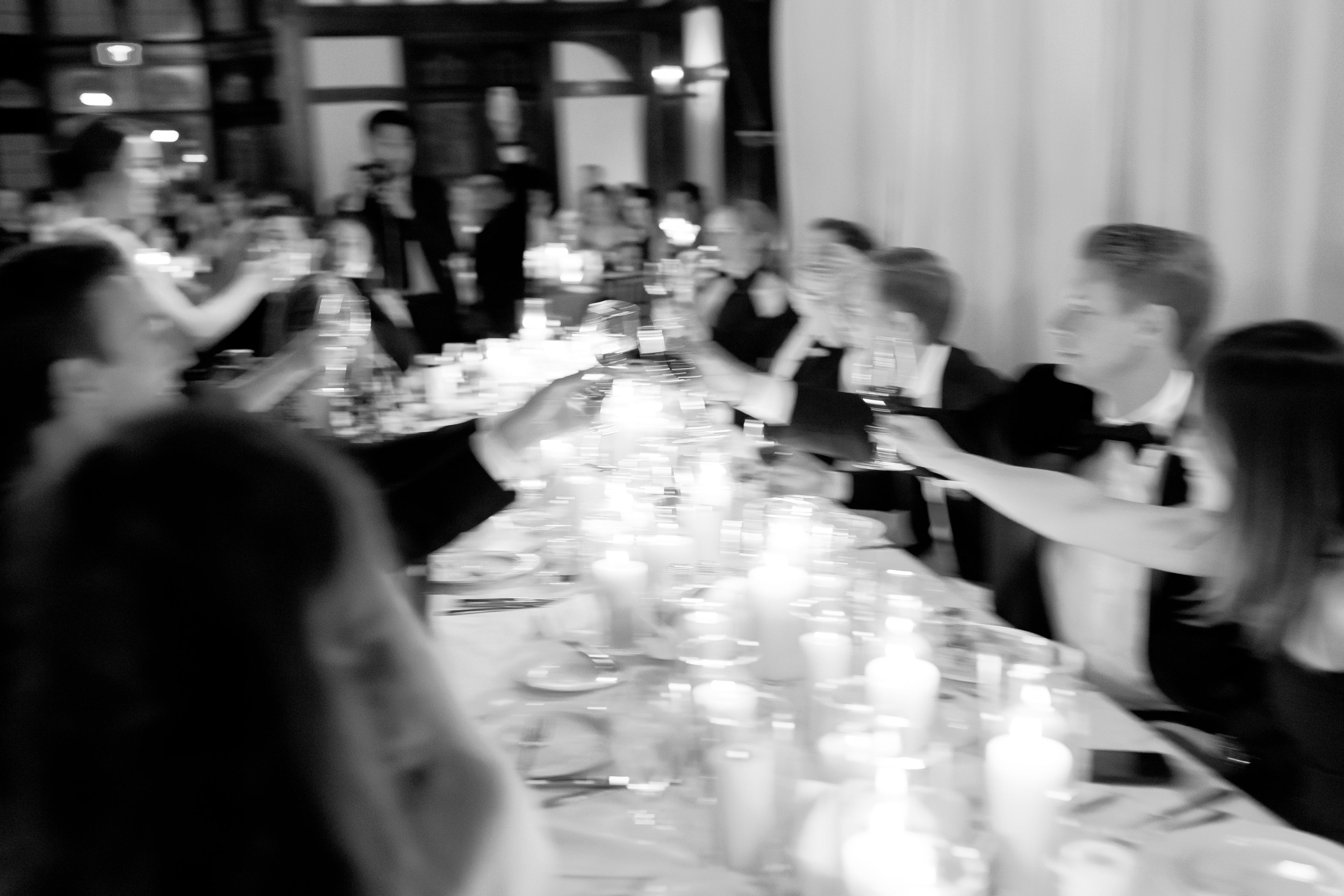 black and white photo of a wedding party clinking wine glasses with a candlelit table