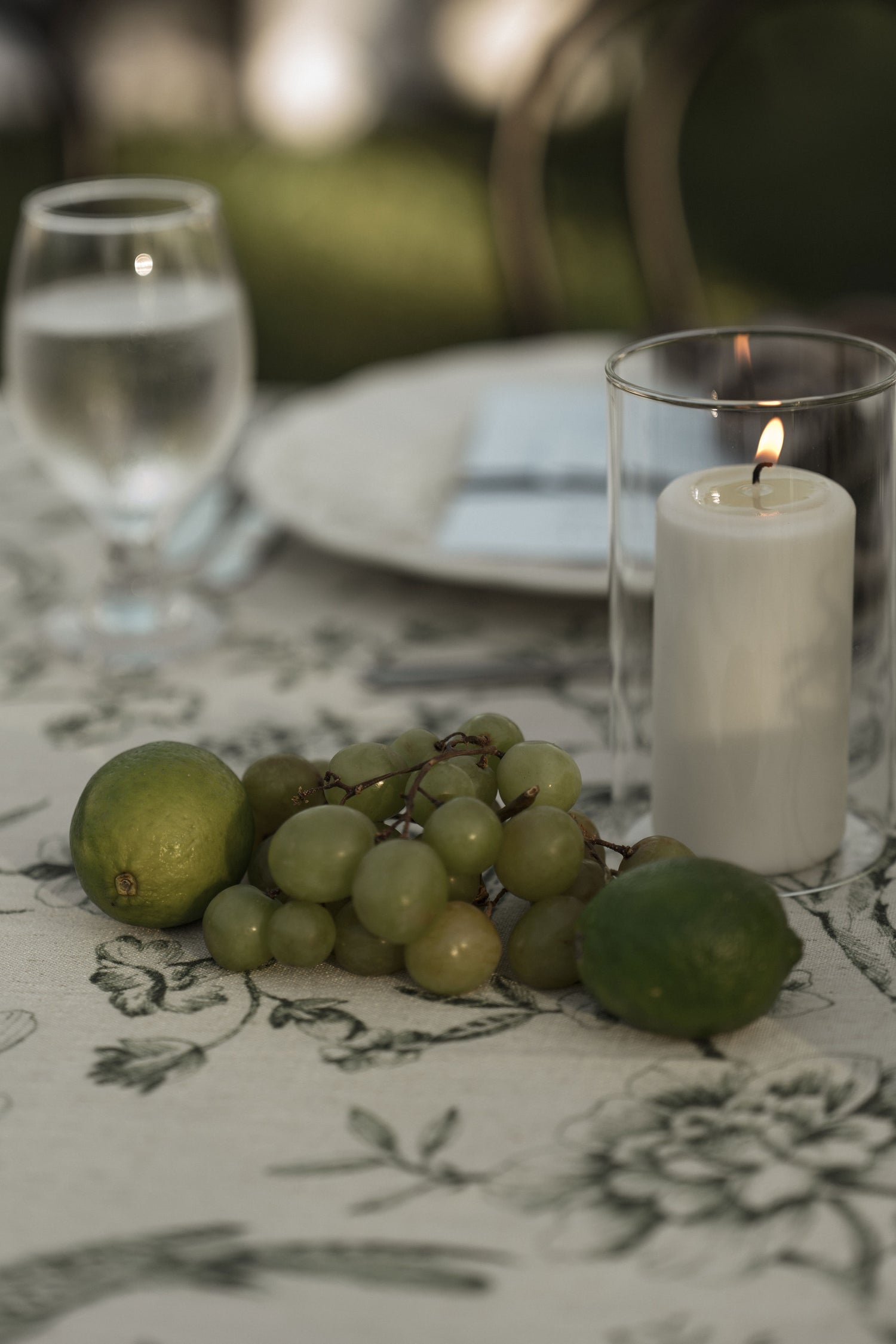 photo of limes, grapes, and a green floral tablecloth with a white pillar candle in a glass hurricane