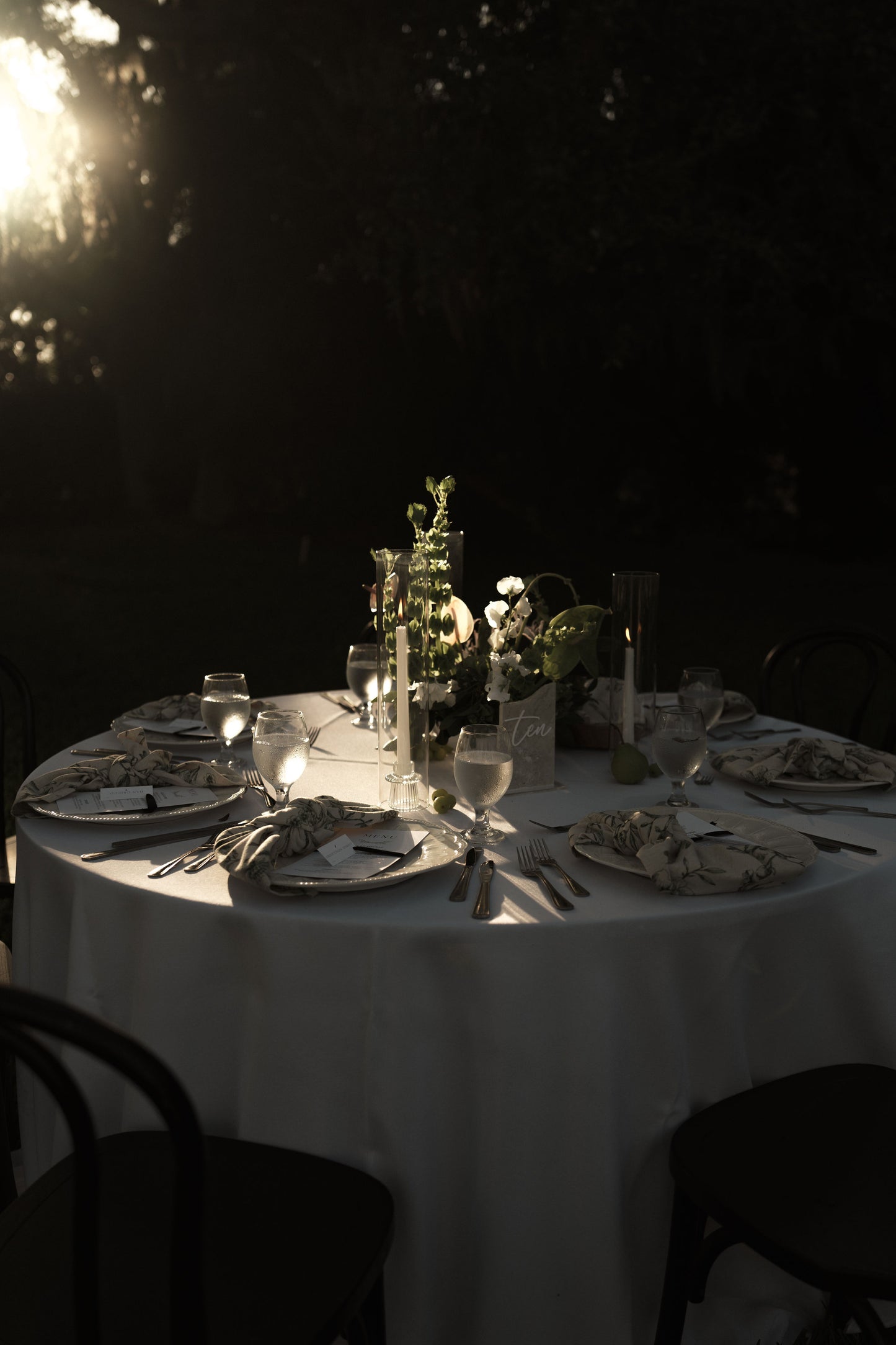 Dining table set for a meal with wine glasses, cutlery, and plates in a dark setting.