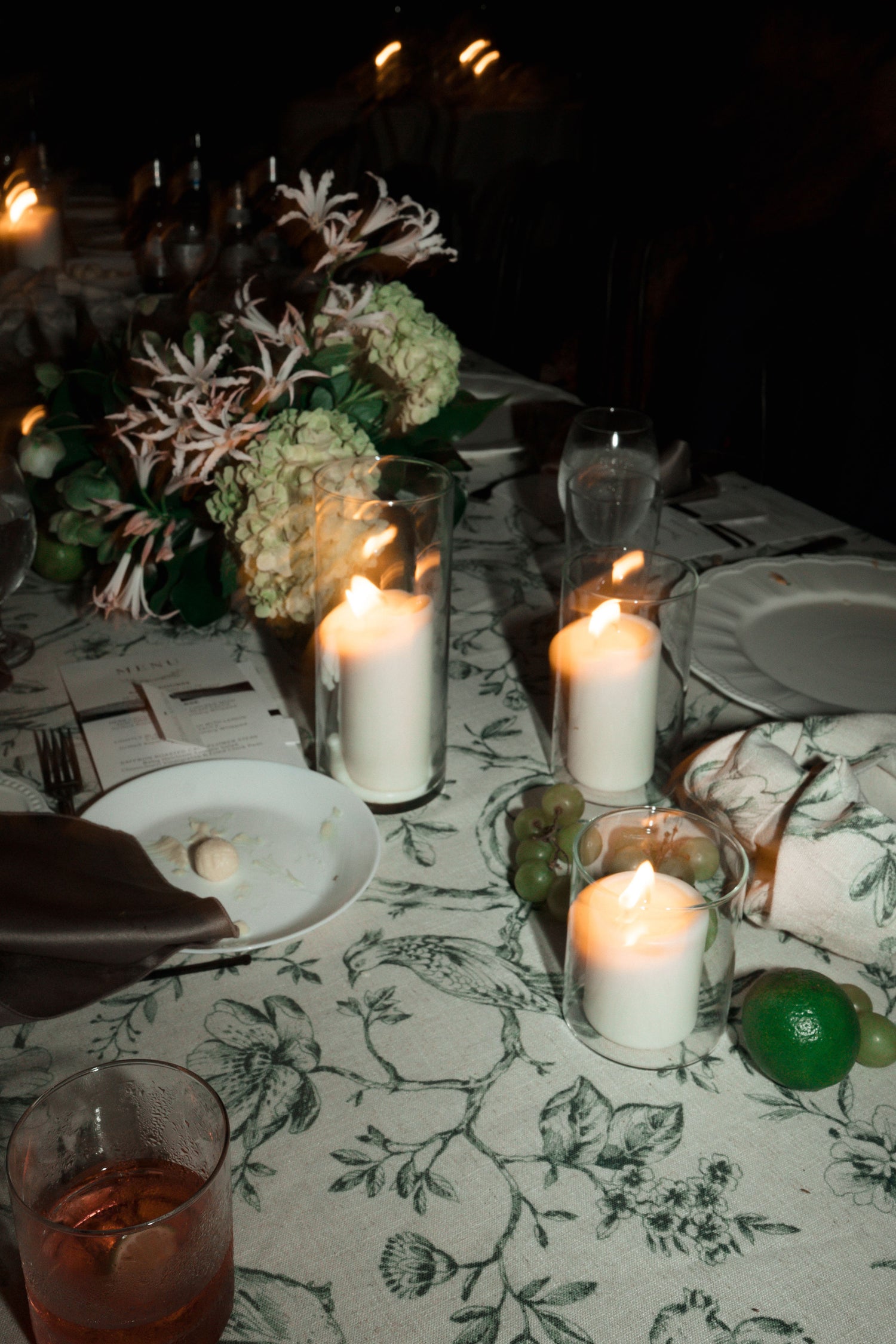 Dining table set for a meal with candles, flowers, and cutlery at night.
