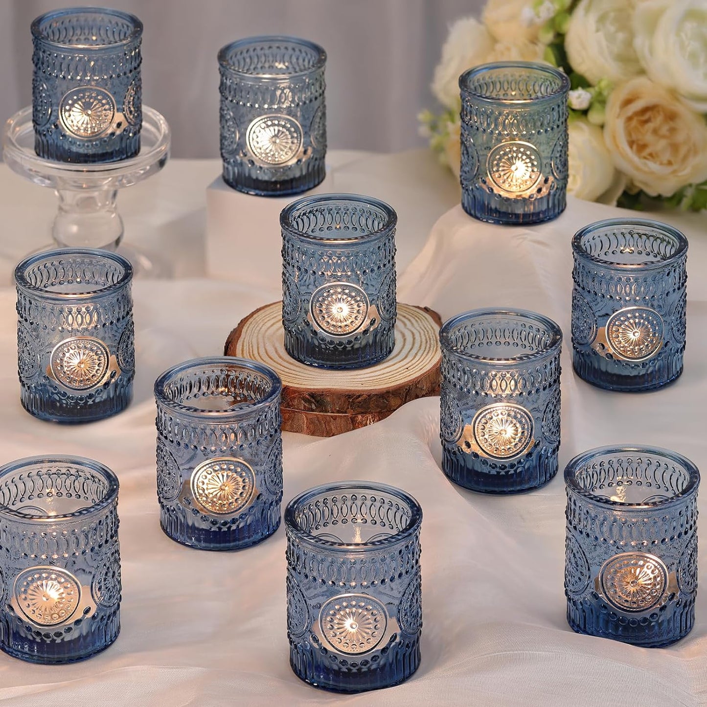 Set of blue glass candle holders with lit candles on a white surface.