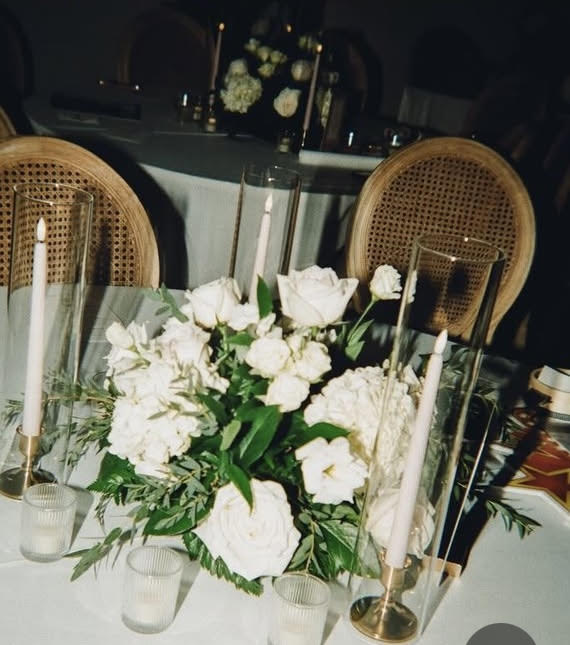 Decorative table setting with white flowers, candles, and greenery on a dark background