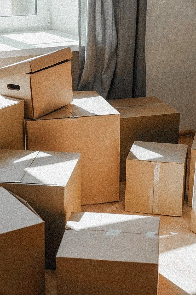 Stack of cardboard boxes in a room with sunlight filtering through a window.