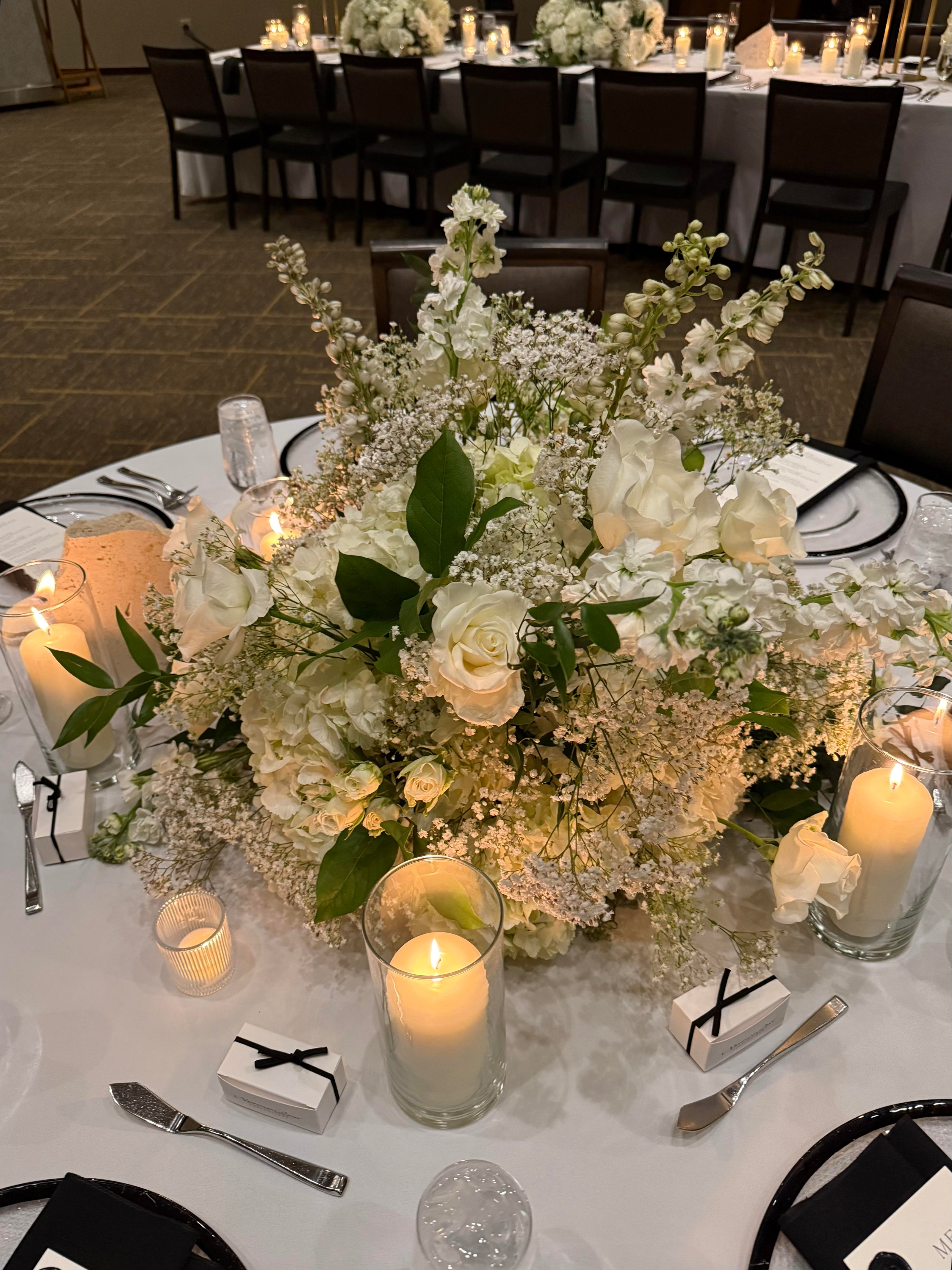 Decorative floral arrangement with candles on a table setting in a formal event venue.